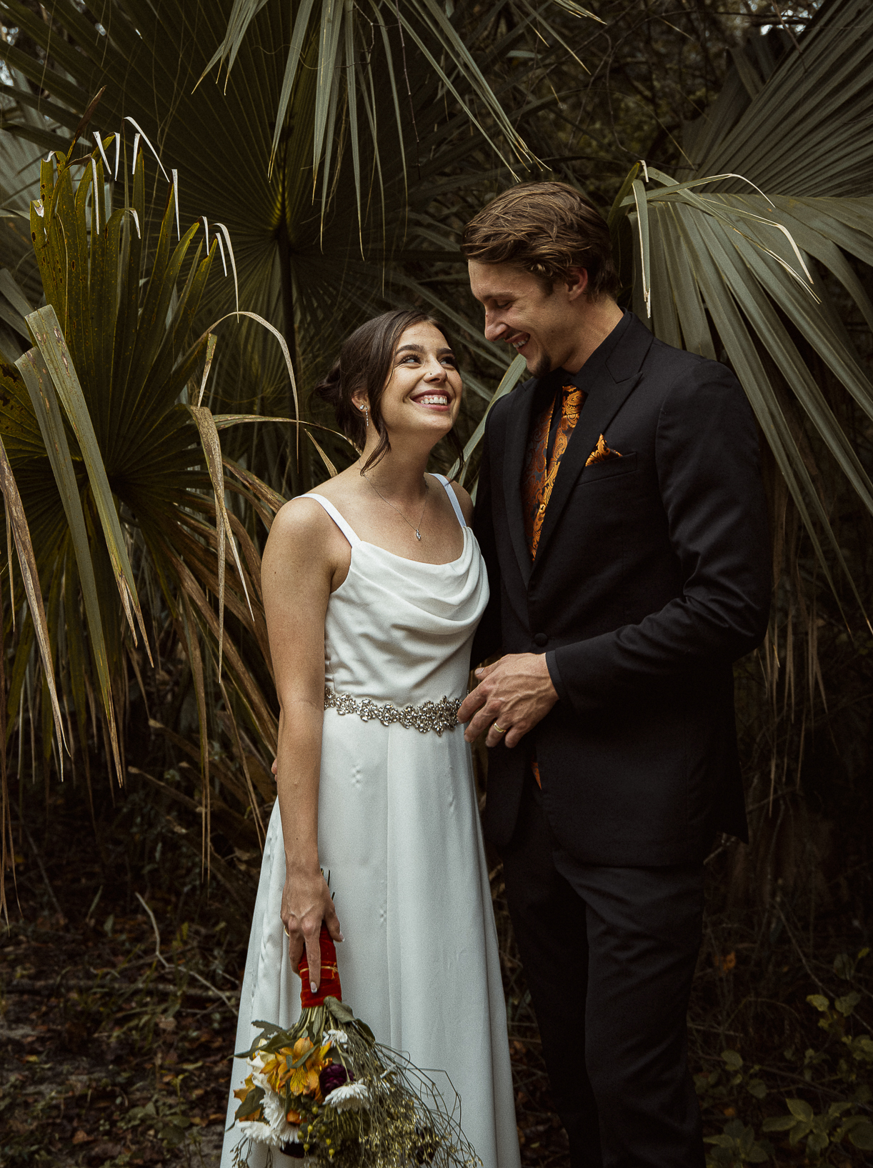Editorial wedding portrait of couple laughing together among palm trees, captured in natural light- romantic St. Augustine wedding photography.