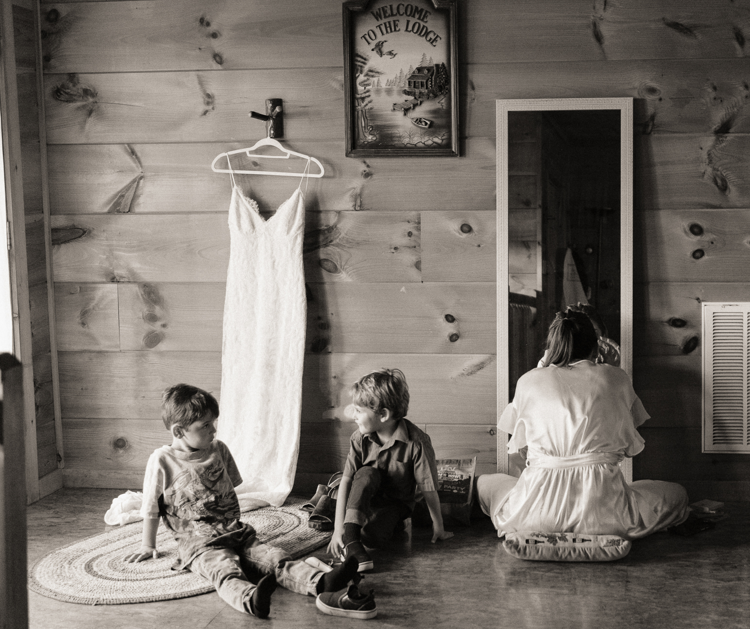 Bride getting ready in room with two young boys next to her, documentary style.