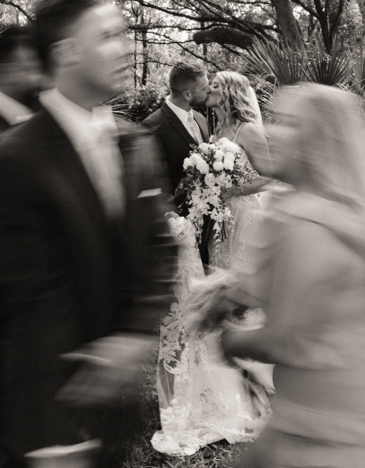 Editorial-style wedding photograph capturing a bride and groom sharing a kiss amid blurred motion of guests passing by- cinematic, documentary wedding photography in St. Augustine.